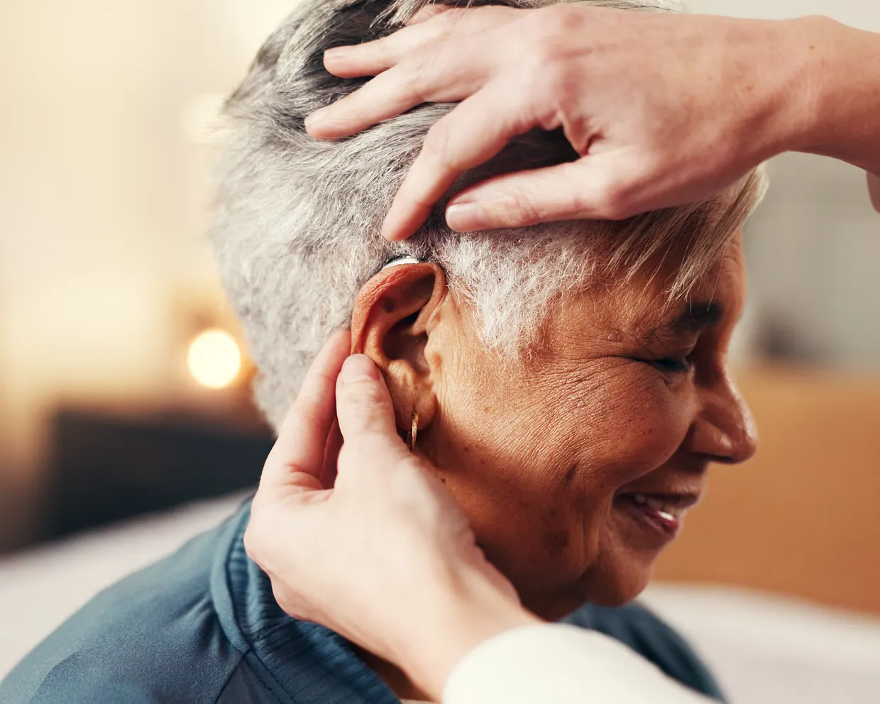 A smiling older woman being fitted with a hearing aid by a clinician